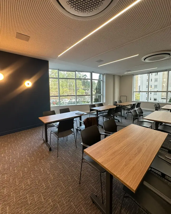 Sala de aula do Instituto AngioGold, com mesas de madeira, cadeiras e janelas amplas com vista para área verde
